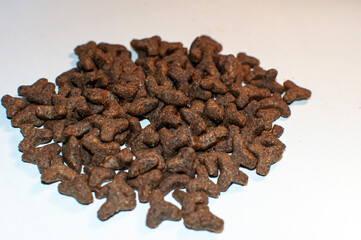 Close-up of dry pet food on a white background. Brown crunchy kibble pieces in various shapes, scattered in a pile. Concept of cat or dog nutrition and healthy feeding