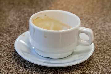 A used white espresso cup sits on a matching saucer, showing coffee remnants against a speckled tabletop background