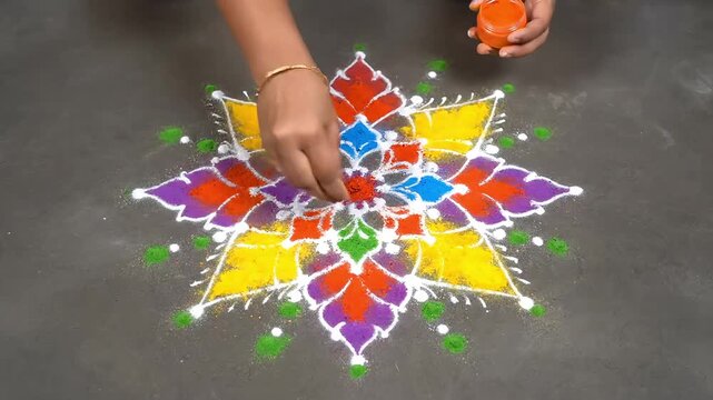 Hands carefully adding colorful powder to create a vibrant geometric rangoli design on a flat surface.