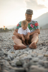 Father holding baby by the sea, playing together in the waves. Tender family moment full of love, care, and joy. Concept of fatherhood, childhood, bonding, and vacation lifestyle outdoors.