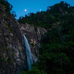 Waterfall cascading down a rocky cliff at twilight under a moonlit sky