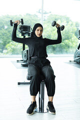 Fototapeta premium Muslim woman in sports hijab lifting dumbbells at gym, focusing on strength training and fitness, symbolizing empowerment, health, active lifestyle and diversity in modern Islamic culture.