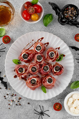 Halloween snacks. Eyeballs cooked from jamon, mozzarella cheese and olives on a plate on a concrete background. Top view.