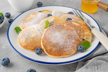 Delicious homemade pancakes with blueberries and honey, sprinkled with powdered sugar on top on a gray concrete background.