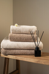 Stack of towels in neutral colors and aroma diffuser in modern aesthetic interior. Fabric bathroom accessories for hygiene, spa and skin care.