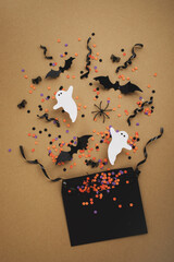 Halloween party composition from envelope with festive decoration from bats, ghosts and confetti on golden background top view.