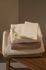 Stack of towels in neutral colors and paper blank in modern aesthetic interior with sunlight shadows. Fabric bathroom accessories for hygiene, spa and skin care.