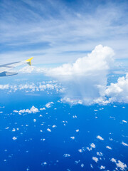 A bright aerial view from an airplane window, showing a yellow-tipped wing against a deep blue ocean and scattered white clouds below