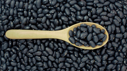 Raw black beans on horizontal wooden spoon over heap of black beans background. Ideal for...