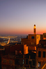 Illuminated mosque minaret above Mardin old town with glowing city lights and Mesopotamian plains...