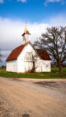 Rustic white barn with red roof, steeple, and cloudy sky