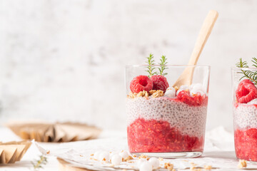 A single glass of layered raspberry and chia seed pudding topped with fresh raspberries and white crowberry on a rustic wooden platter