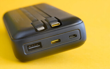 Close-up of a high capacity power bank with built-in USB-C and Lightning cables, plus USB-C and USB-A ports, on bright yellow background; gadget charging device. Photo