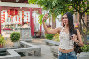 Young Asian woman in traditional Asian garden park during summer taking selfie with phone