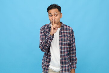 Portrait of a handsome young man looking at the camera with a smile, a finger gesture covering his...