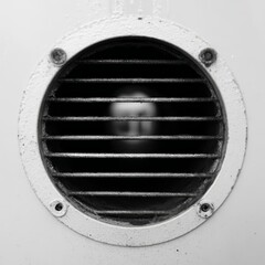 Close up of a round black metal ventilation grate with horizontal slats on a white surface