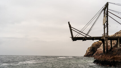 Fototapeta premium Old abandoned industrial pier on a rocky cliff over a moody sea