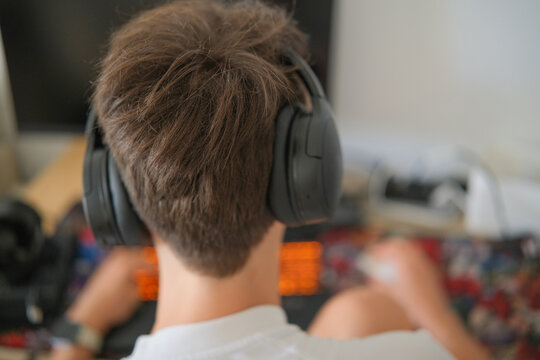 Teenage boy with headphones playing video games on laptop computer at home - Powered by Adobe