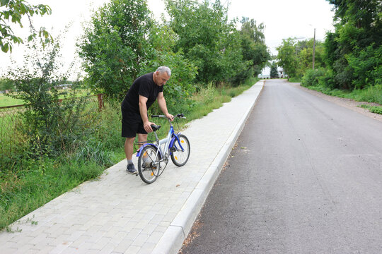 Man bending over bicycle, holding handlebars and trying to spin wheels on roadside.