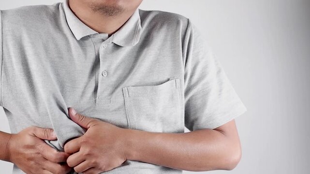 A young Asian man in a gray shirt is experiencing right-sided chest pain. This chest pain can be caused by a heart attack, myocardial infarction or ischemia, myocarditis, pneumonia, stress, etc.