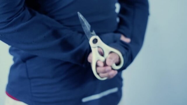 Rear view of a maniac hiding a scissors behind his back. Halloween, horror.Close up, back view of armed man, holding the knife in his hands, hiding it behind his back. Concept of violence, murder
