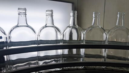 A close-up shot of a set of six empty glass bottles arranged on an assembly line in a factory