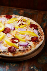 Pizza with chorizo ​​sausage, mozzarella cheese and yellow pepper. Rustic wooden background. Soft focus.	