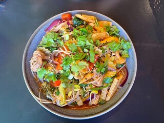 A mix of Asian cuisine, overhead view: noodles in tomato sauce with mini corn, mushrooms, peppers, cilantro, and daikon