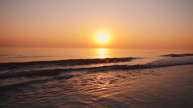 Low angle shot of of small waves crashing on shore during sunset at Mandvi, Kutch, India. Beautiful beach with orange setting sun. Summer vacation background. Travel and holidays concept.