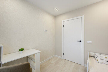 Bright room featuring a desk, white door, and light wood flooring. Minimalist design with neutral tones