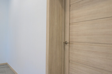 A light wood door stands against a white wall, featuring a simple, modern design with horizontal panels. A metal handle is visible