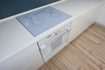 A clean, modern kitchen countertop with a gray stovetop, a white oven, and light wood flooring.