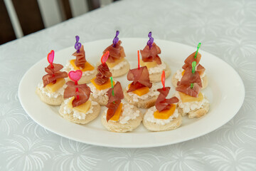 Delicious small snacks are arranged on a white plate, topped with slices of meat, cheese, and colorful decorative picks. This appealing display is perfect for a festive occasion.