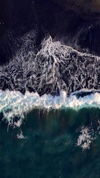 Aerial looking down at waves on a black sand beach in Bali Indonesia. Vertical Video.