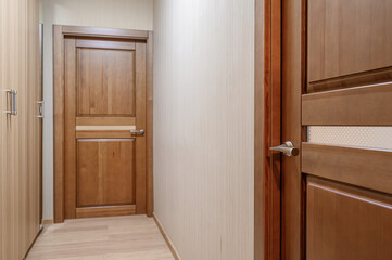 A hallway with light-colored wooden doors, beige walls, and light wood flooring. Focus on wooden details and hardware