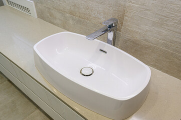 modern bathroom sink with a sleek, white oval basin and a chrome faucet, set against a neutral tiled backdrop