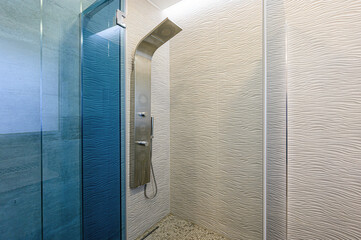 A modern shower area with textured walls, a sleek shower panel, and a blue-tinted glass partition