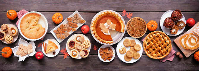 Autumn desserts table scene. Table scene with a collection of traditional fall sweet treats. Above view over a dark wood banner background. Copy space. Pies, pumpkin roll, muffins, cookies.