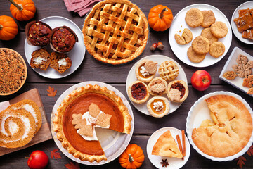 Autumn desserts table scene. Table scene with a collection of traditional fall sweet treats. Above view over a dark wood background. Copy space. Pies, pumpkin roll, muffins, cookies.