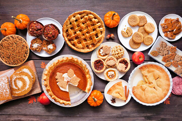 Autumn desserts table scene. Table scene with a collection of traditional fall sweet treats. Above view over a dark wood background. Copy space. Pies, pumpkin roll, muffins, cookies.