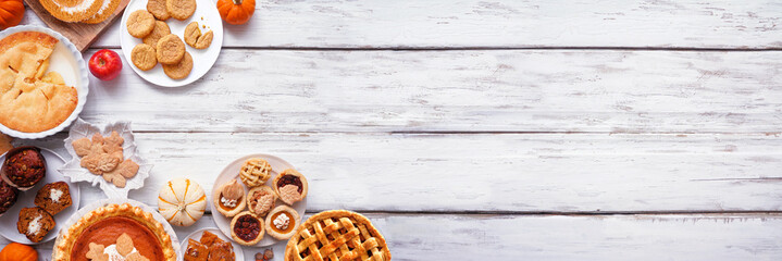 Autumn desserts corner border. Table scene with a collection of traditional fall sweet treats. Above view over a white wood banner background. Copy space. Pies, pumpkin roll, muffins, cookies.