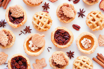 Autumn pie theme dessert background. Top view against a white marble background. Pumpkin, apple and pecan mini pies.