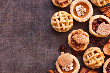 Autumn pie theme dessert side border. Overhead view against a dark stone background. Pumpkin, apple and pecan mini pies.