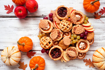 Fall pie theme dessert board. Top down view table scene against a white wood background. Pumpkin, apple and pecan mini pies, snickerdoodles and pumpkins rolls.