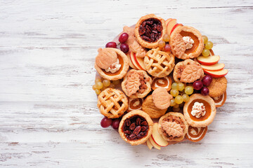 Autumn pie theme dessert board. Overhead view against a white wood background. Pumpkin, apple and pecan mini pies, snickerdoodles and pumpkins rolls.