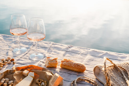 Two glasses of rose wine with cheese and nuts on a pier at sunset.