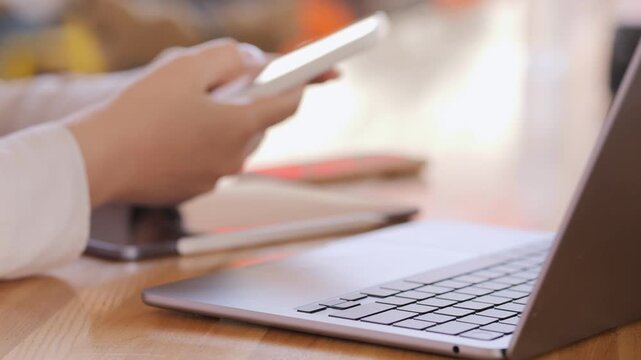 Person is using a laptop and a cell phone. The laptop is open and the cell phone is in the person's hand