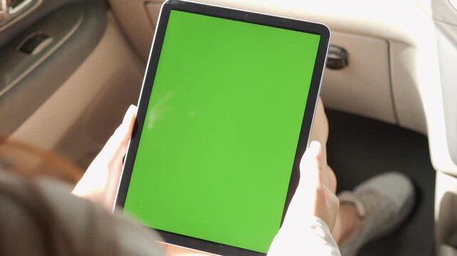 Person is holding a tablet with a green screen. The tablet is in a car. The person is wearing white shoes
