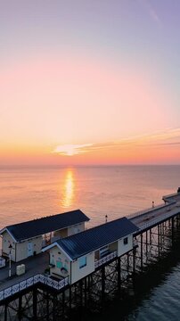 Aerial drone footage of sunrise above Penarth pier. Vertical ascending shot.