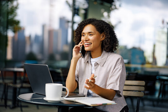 A professional woman enjoying a coffee while on a phone call, working on her laptop in an urban cafe.